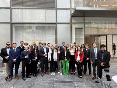 USD students stand in front of NYC businesses, in professional attire, and smile for the camera.