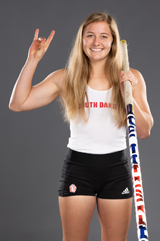 Alayna Falak holds up the 'Go Yotes' sign on her hand. She is wearing her track uniform and holding a pole for pole vault.