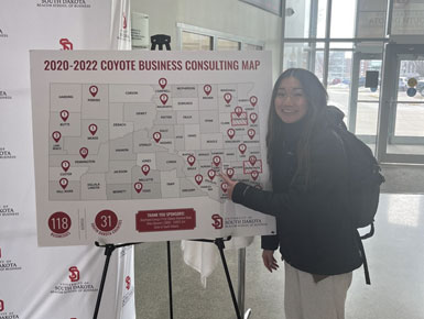 A student points to a South Dakota county on a physical map, showing where $5 was gifted toward the Beacom School of Business during Unite for USD