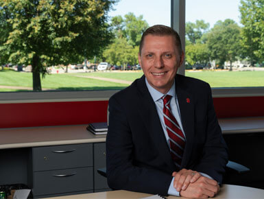 Klaus Beckmann, Ph.D., interim dean of the Beacom School of Business, sits in an office setting, smiling at the camera. He is wearing a suit.