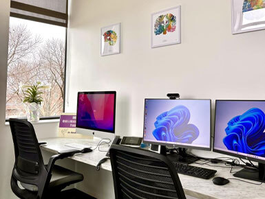 A closeup of the CAST Lab workstations, equipped with computer chairs and monitors. There is also artwork above the computer monitors.