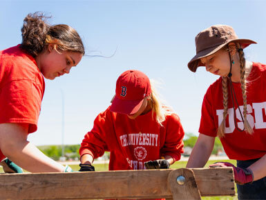 Three USD students run dirt through a sifter to see if they can find any artifacts.
