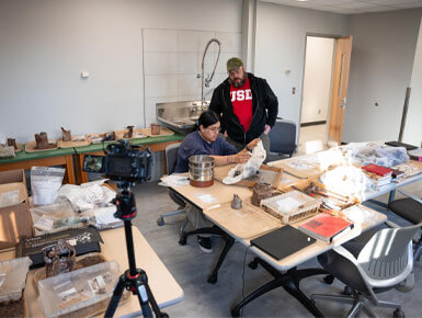 Angel Vazquez, a USD archaeology student, sits in the new ARCHLAB with a faculty member overlooking his findings. 