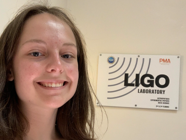 Oleksandra Lukina smiles for a selfie in front of a sign that says LIGO.