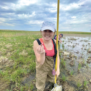 Ella Wittmuss, B.S. ’25, medical biology alumna, stands in a field, holding wildlife.