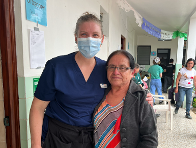 Lindsey Jorgensen, who is wearing a face mask and scrubs, smiles for a photo with an audiology patient at a clinic in Guatemala.