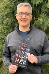 A portrait of Joshua Moehling holding his book "And There He Kept Her."