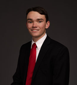 Griffin Petersen posing for headshot photo in front of dark gray wall