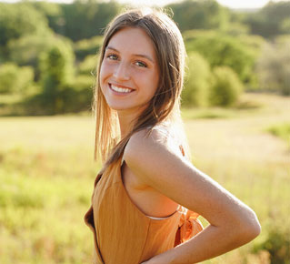Kayla Vohlken poses for photo looking over shoulder in grass field with sun shining 