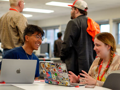 Ariestotle Raj Maharjan and Margaret Kathol sit at a table with their laptops in front of them, working together during the USD Hackathon.