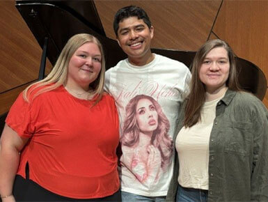 Three out of the four USD students, who have advanced to the semifinal round of the National Student Auditions, stand on a stage in front of a grand piano.