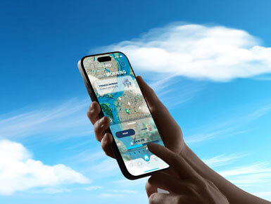 This photo, set against a blue background with white clouds, shows a rendering an arm/hand, holding a cell phone that has the OKO app on it. The cell phone displays a "Good Morning" message, with a summary of the forecast for the day.