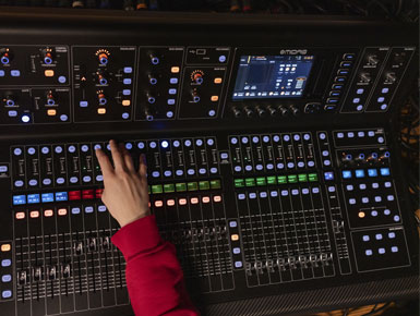 A hand hovers over a sound board, working the sound levels of a performance.