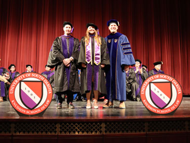 Holly Tofte stands on the stage during the hooding ceremony at the Knudson School of Law's graduation ceremony.