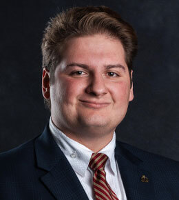 Vincent Tarallo smiles for his professional photo, wearing a dark suit and a red and gold striped tie.