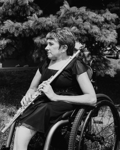 A person in a wheelchair holds a flute and looks off to the side.