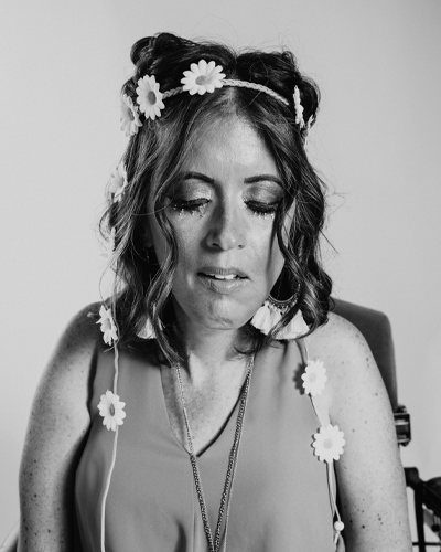 A person wears a daisy flower headband and necklace and looks downward.