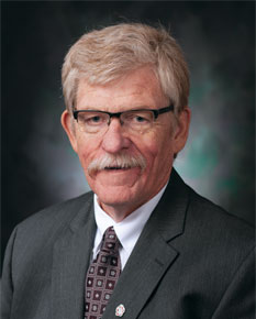 Gerald Yutrzenka posing for headshot in front of gray wall