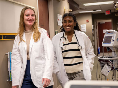 Two USD SSOM students walk down the halls of the Coyote Clinic. They are smiling at the camera.