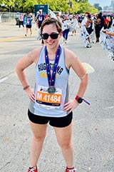 Photo of Meredith Reynolds after completing a half marathon wearing a runners bib and a completion medal. 