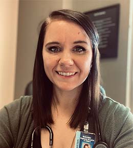 Emily Boden, M.D., a 2015 USD Sanford School of Medicine graduate, stands with a stethoscope around her neck, smiling at the camera in a professional setting.
