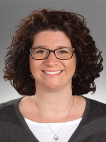 Amy Heisinger posing for headshot in front of gray wall