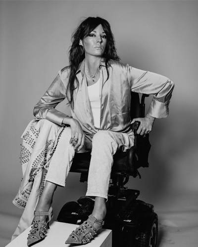 A person in a wheelchair leans forward and holds a powerful pose. Their feet are on a pedestal. 