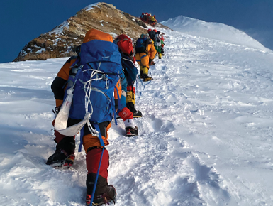 Several people in climbing gear climb up the side of a snow-covered mountain.