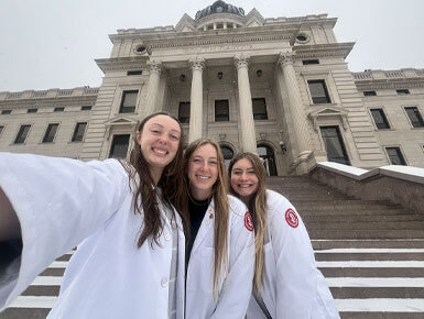 Ruby Hawks, Mariah Block and Jada Tschetter stand in front of the state Capitol.