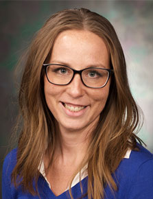 Erin Srstka posing for headshot in front of gray wall