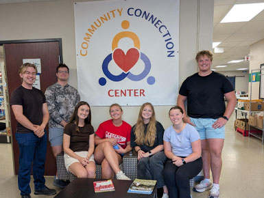 USD Sanford School of Medicine students stand in a hallway, posing for a picture in front of a flag that says, "Community Connection Center."