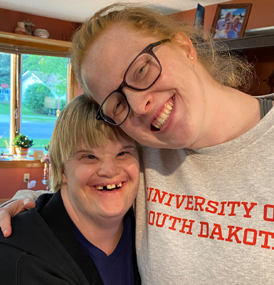 Two people smile for a selfie. They rest their heads on each other.