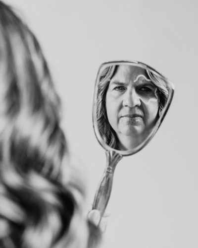 A handheld mirror shows the reflection of a person looking into it.