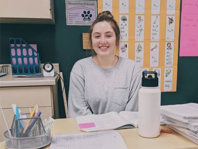 Alisa Larsen sits behind her teacher desk and smiles. 
