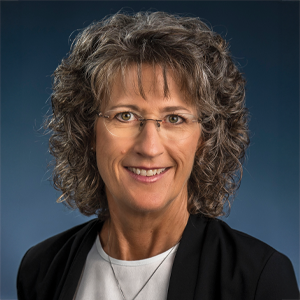 Pamela Homan, Ed.D. ’96, sits forward with her back against a blue background, looking at the camera and smiling.