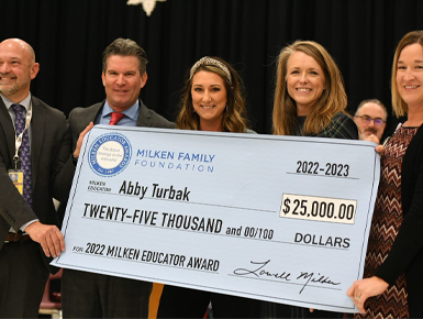 A group of five people holding a large check for 25 thousand dollars.