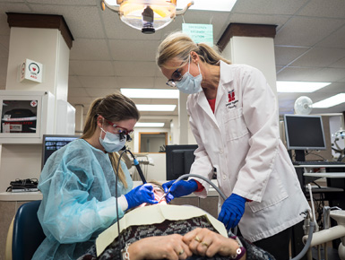 A dental hygiene faculty member and a student check on a patient's teeth in a dental office.
