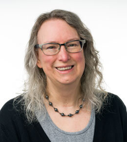Melissa Berninger smiles at the camera for her professional photo, on a white background. She is wearing a gray and black shirt and glasses.
