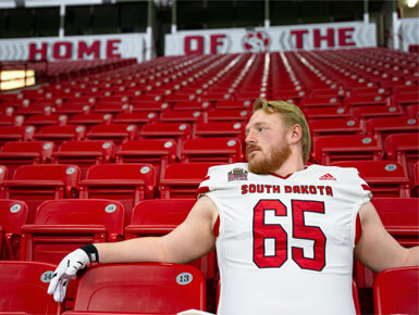 Caden Ellingson sits in the stands inside the DaktoaDome, looking off to his right.