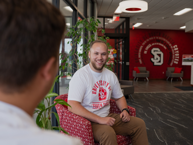 Two students sit face to face and engage in conversation in the Wagner Welcome Center.