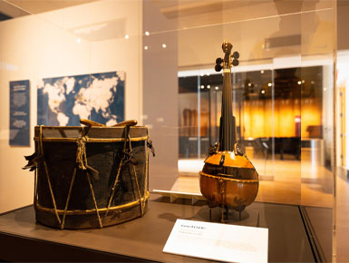 The Gourd Fiddle sits in a display case, next to a drum in the National Music Museum.