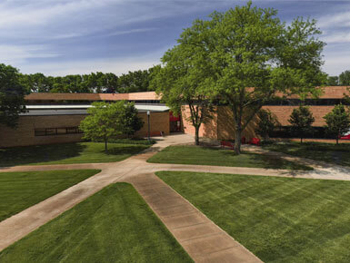 An aerial shot of the Knudson School of Law building, which is housed on the USD campus. In the forefront are two different pathways of sidewalk, patches of grass and green trees.