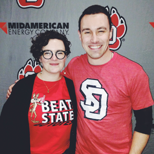 Erin Muckey Patel '10 poses with her brother, Erik Muckey '14. Both are wearing USD shirts with a USD background.