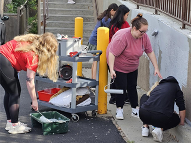 Five students paint a cement wall. 