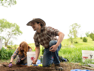 Two students kneeling on the ground, digging through dirt to find remnants.