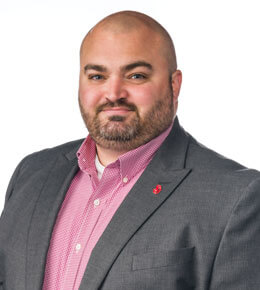 USD Police of Chief, Bryant Jackson, poses for his headshot photo. He is wearing a gray blazer with a red checkered shirt underneath. He is smiling at the camera.