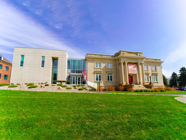 The National Music Museum sits on the USD campus on a sunny day, surrounded by green grass and plants.