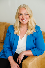 Sadie Swier wears a cobalt blue blazer while sitting on a couch and smiling. 