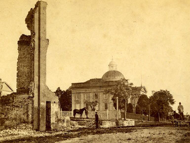 This historical image shows a run down building with an individual standing next to it. The image is from the Mississippi Department of Archives and History.