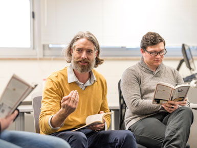 Joseph Tinguely sits on a chair in a circle of students and lectures about a book.